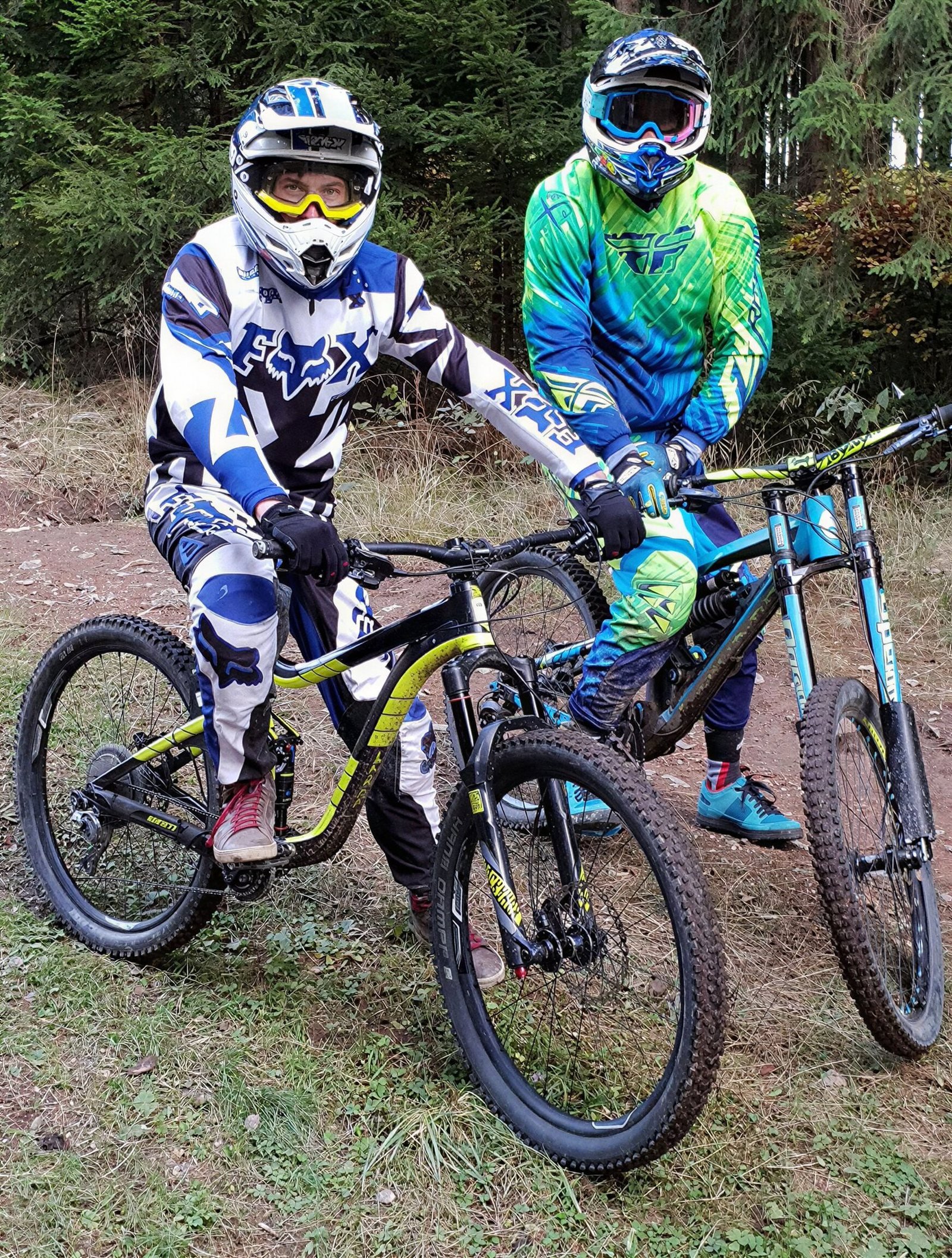 Zwei Mountainbiker in voller Schutzausrüstung im Wald.